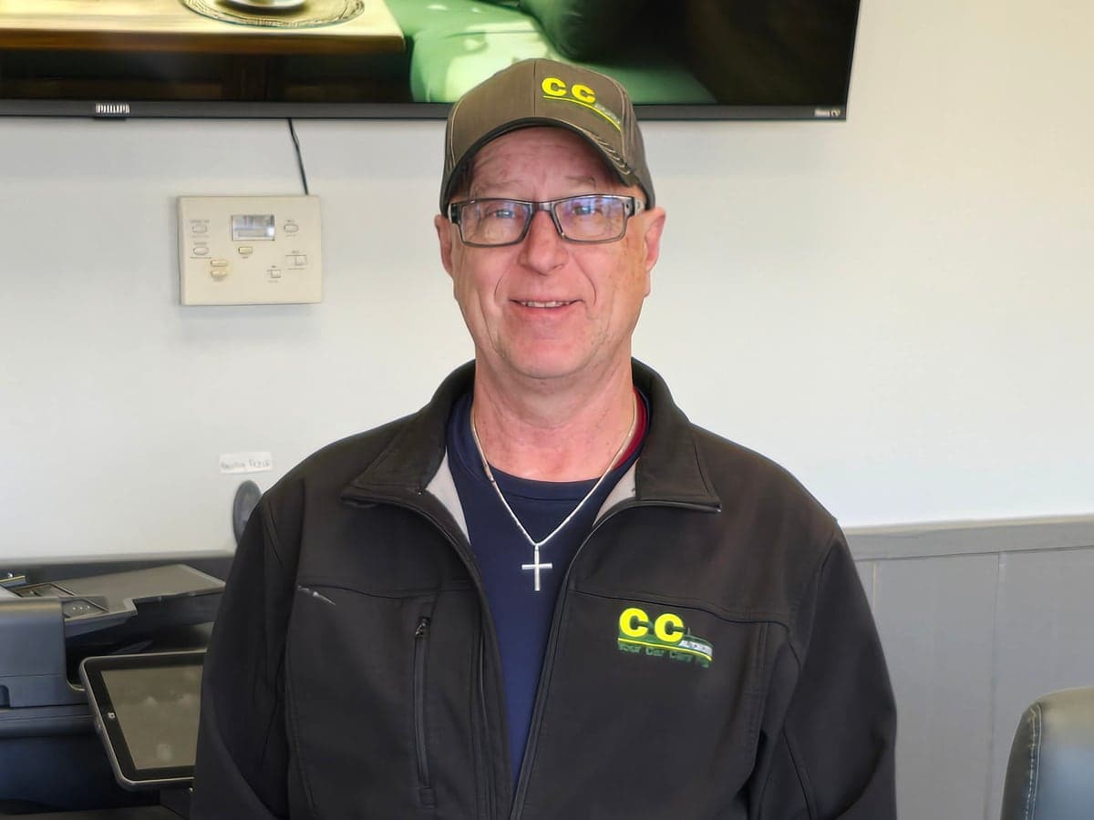 Dan, in a C&C Automotive jacket and cap, at the front counter of the Aiken shop.
