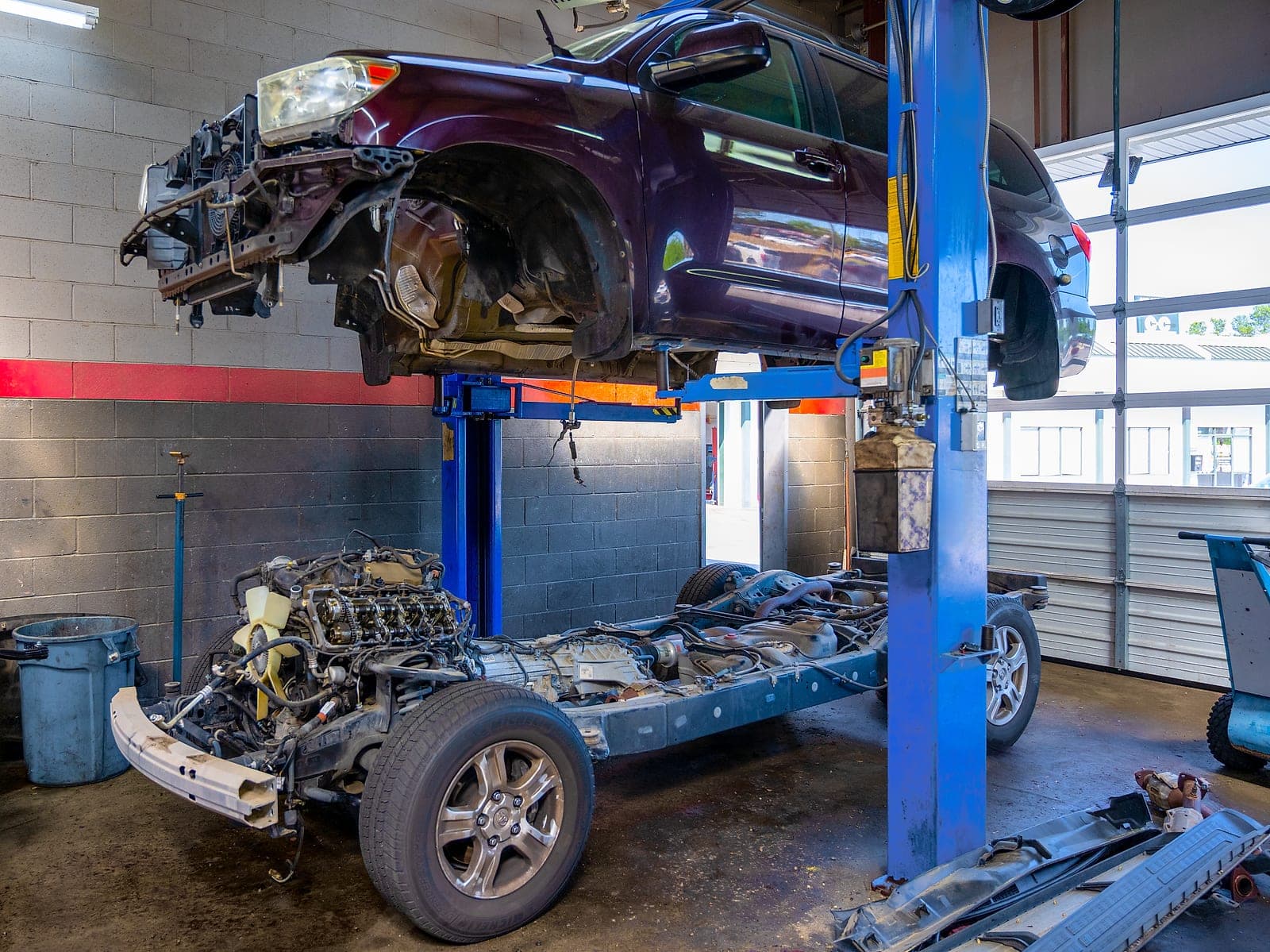 A vehicle body raised on the two-post lift at the Martinez shop with its chassis and drivetrain on the floor below, mid-way through a major repair.