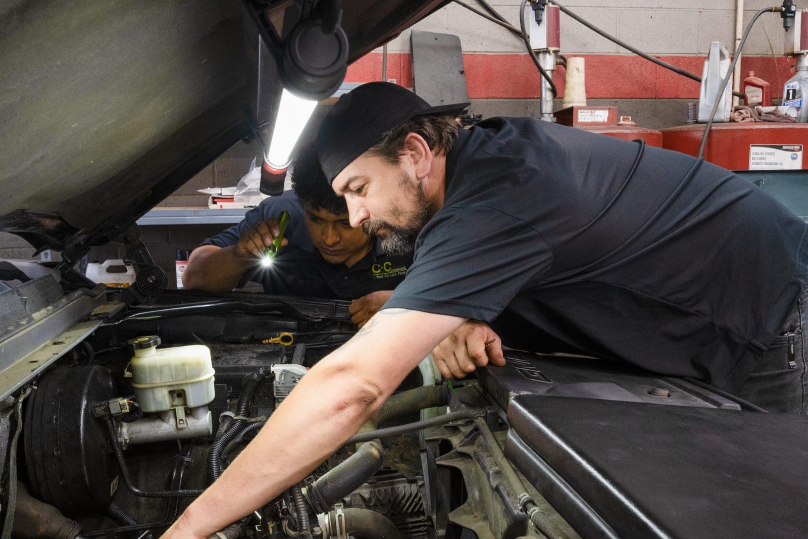 Two C&C Automotive technicians working together under the hood of a GMC at the Martinez shop.
