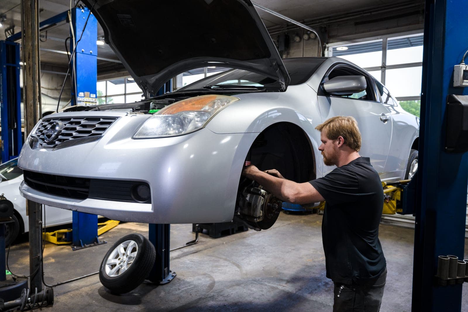 Technician servicing the front brakes of a car on a two-post lift at the West Augusta shop.