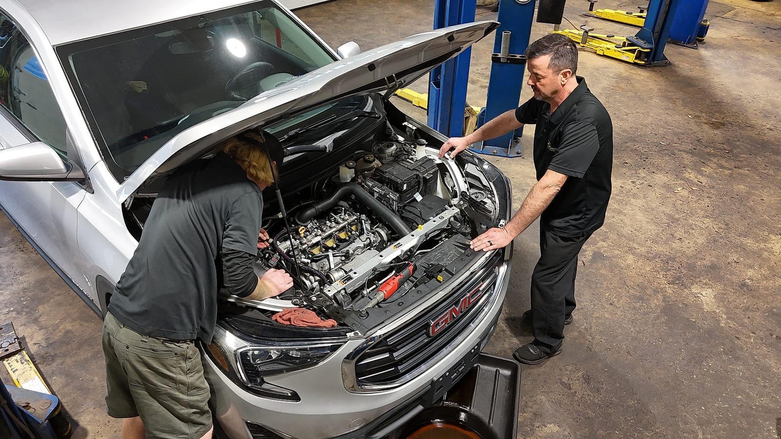 Two C&C Automotive technicians working under the hood of a GMC SUV in the West Augusta service bay.