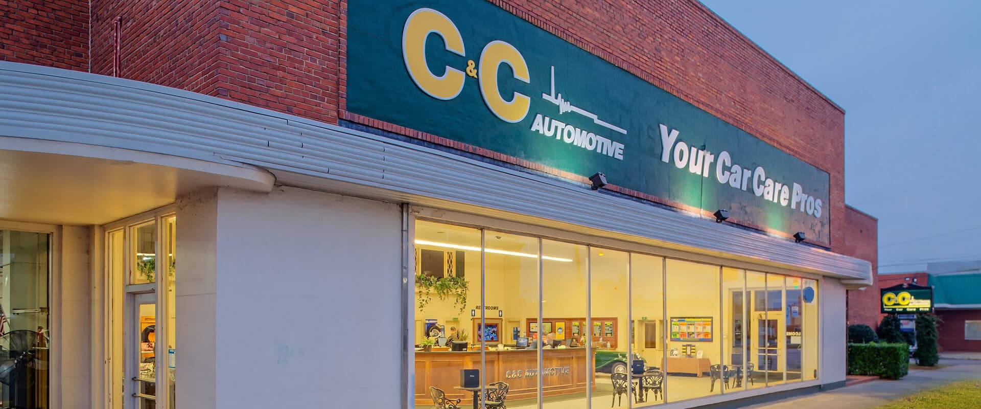 The C&C Automotive shop at 990 Telfair Street in downtown Augusta at dusk, its curved streamline-moderne canopy lit and the front office visible through the windows