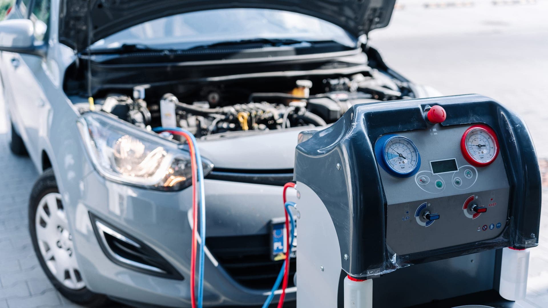 An air conditioning recovery and recharge machine connected to a car's A/C service ports with the hood up